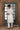 Man wearing a white kurta with white pants standing in front of a decorative frame.