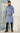 Man wearing a light blue kurta with dark pants standing in a room with a white wall and glass door.